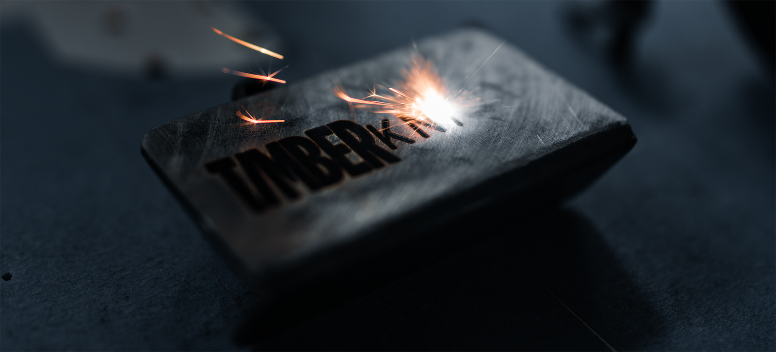 A laser engraving the Timber Knives logo into a blade, throwing sparks